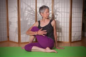 laurel sitting on yoga mat looking right and holding knee stretching to the left