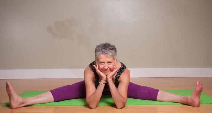 Laurel smiling sitting on yoga mat with legs spread out and elbows on the floor